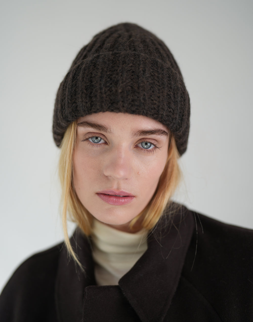 a woman in a brown chunky ribbed beanie and a white turtleneck and brown wool coat #color_brown