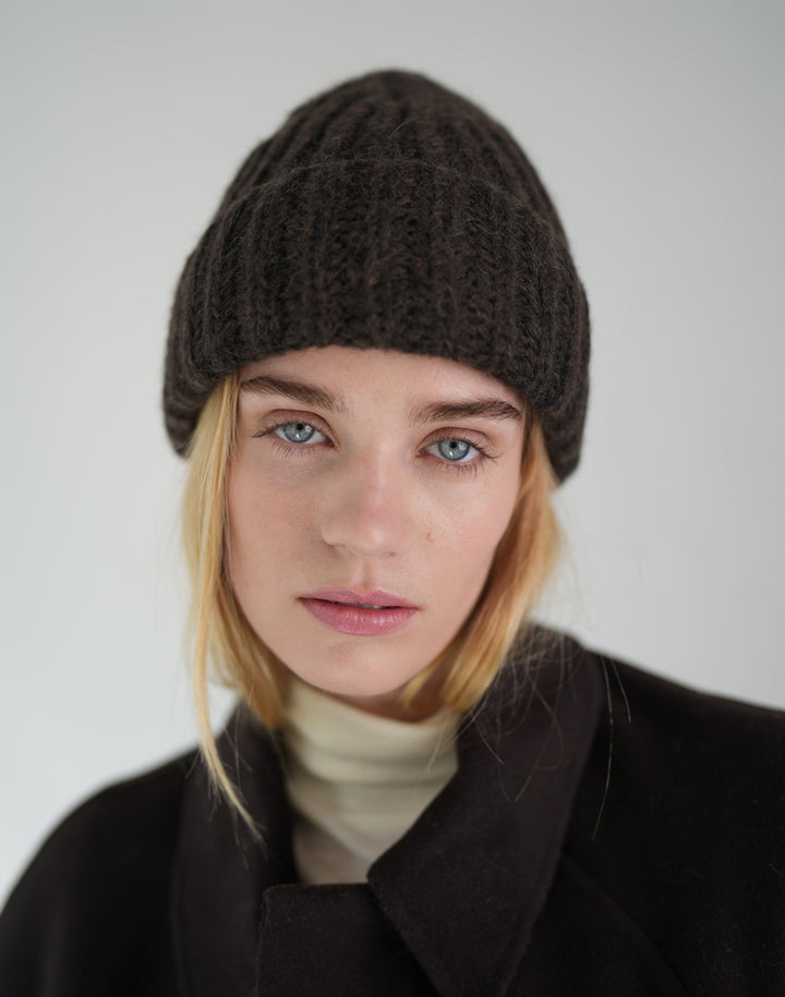 a woman in a brown chunky ribbed beanie and a white turtleneck and brown wool coat #color_brown