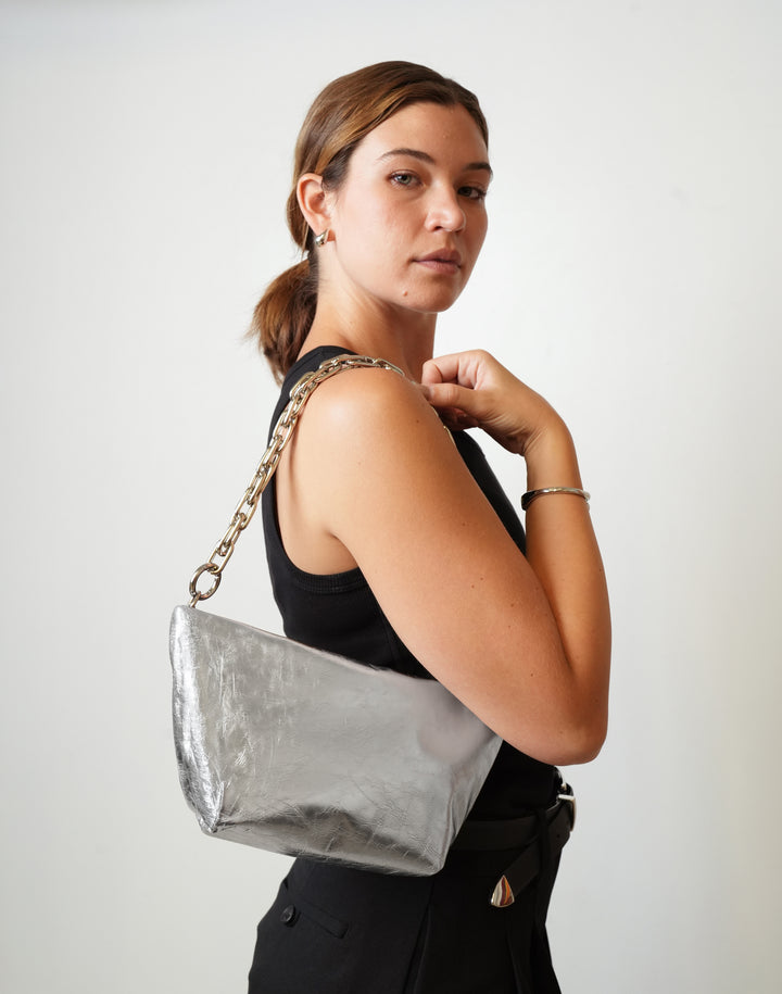 A person in a black tank top and black pants carries a HYER GOODS La Sala metallic silver shoulder bag with a silver chain strap on her shoulder #color_silver