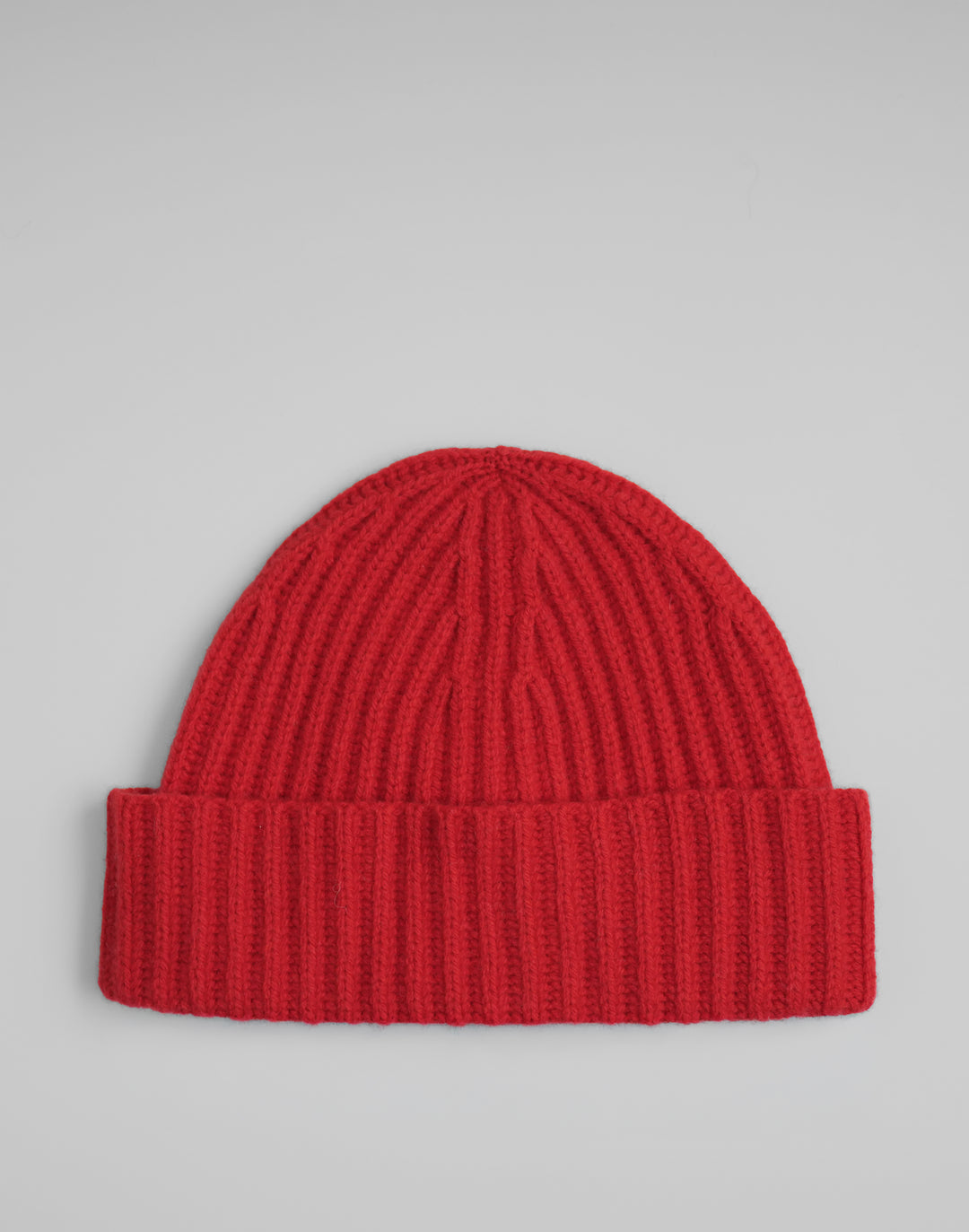 A bright red ribbed knit beanie hat with a folded cuff, photographed flat against a light gray background. #color_red