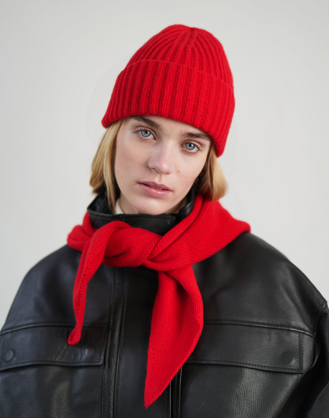 a woman wears a black leather jacket and a matching red ribbed beanie and a bandana scarf tied around her neck #color_red