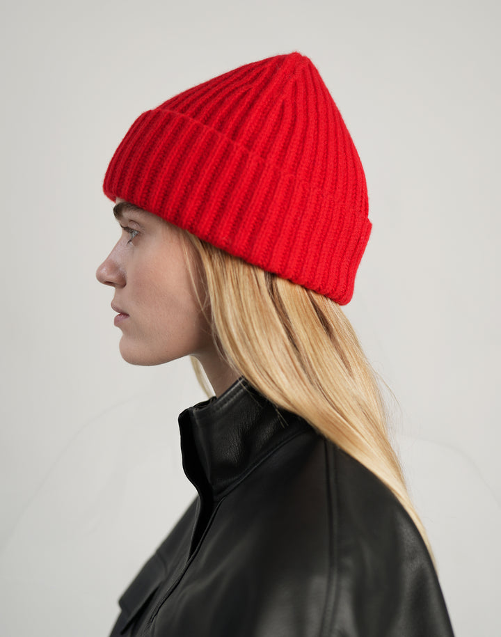 profile shot of a woman in a red ribbed beanie and a black leather jacket #color_red
