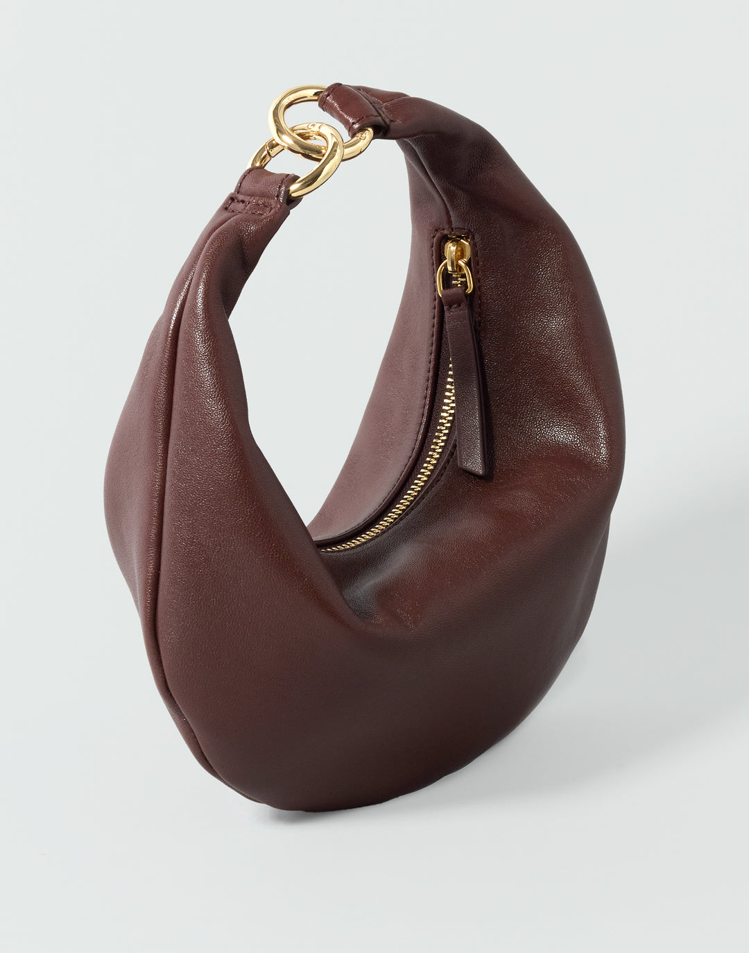 A reddish brown leather crescent-shaped shoulder bag with gold-tone hardware, displayed on a light gray background. #color_bordeaux-vintage