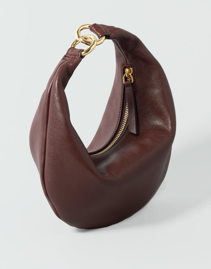 A reddish brown leather crescent-shaped shoulder bag with gold-tone hardware, displayed on a light gray background. #color_bordeaux-vintage