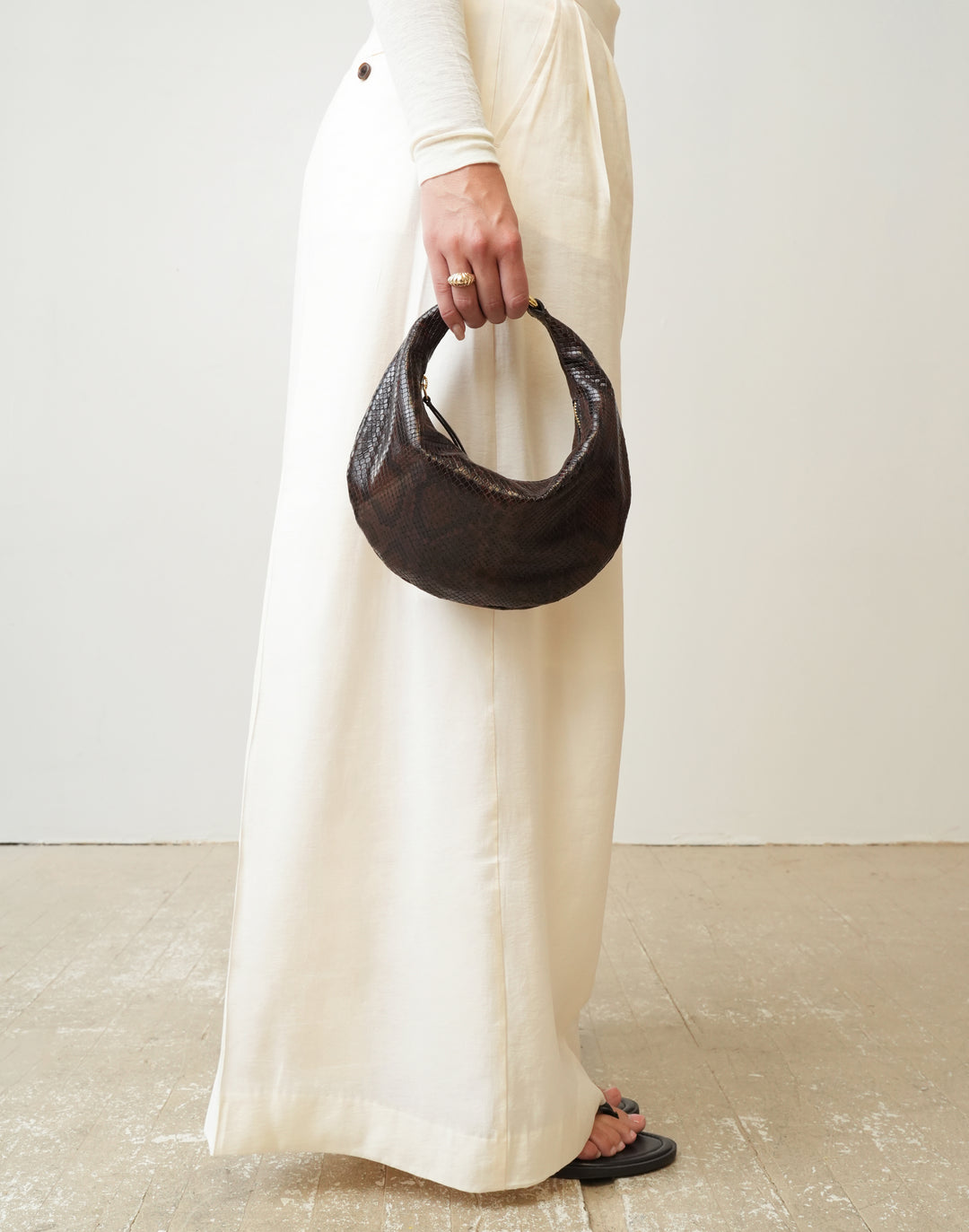 a woman wearing a cream pants holds a HYER GOODS Mini crescent micro ring bag brown python #color_brown-python-embossed