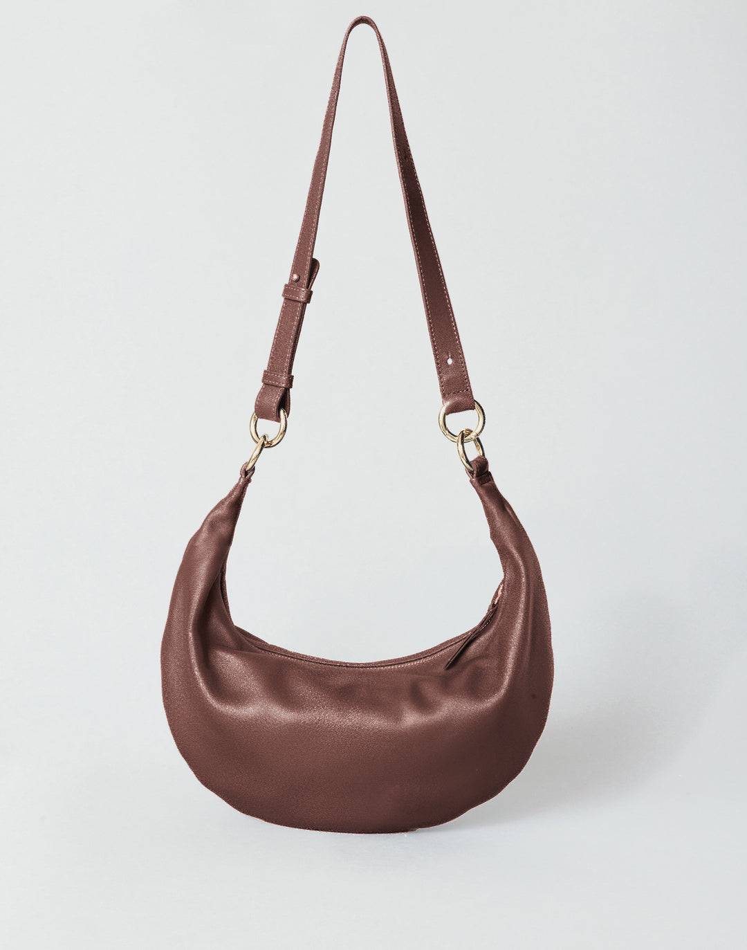 A reddish brown crescent-shaped crossbody convertible crescent bag made of a vintage nappa, featuring a matching adjustable shoulder strap with gold-tone hardware, set against a light gray studio background.#color_bordeaux-vintage