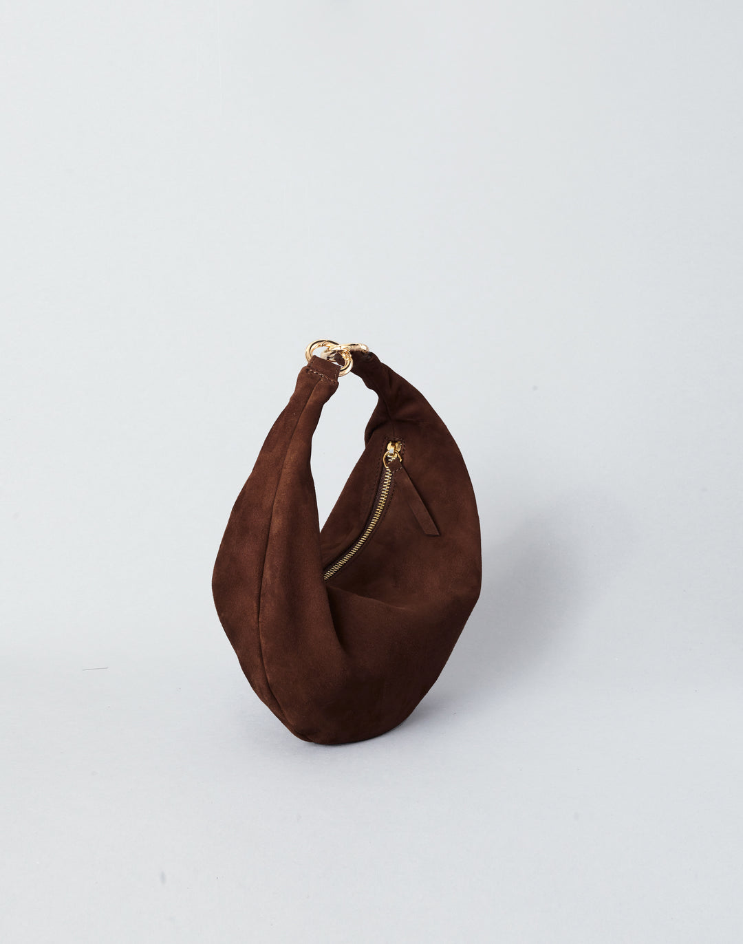 A dark brown suede crescent-shaped shoulder bag with a gold-tone zipper and ring hardware, photographed on a clean light gray background.#color_chocolate-suede