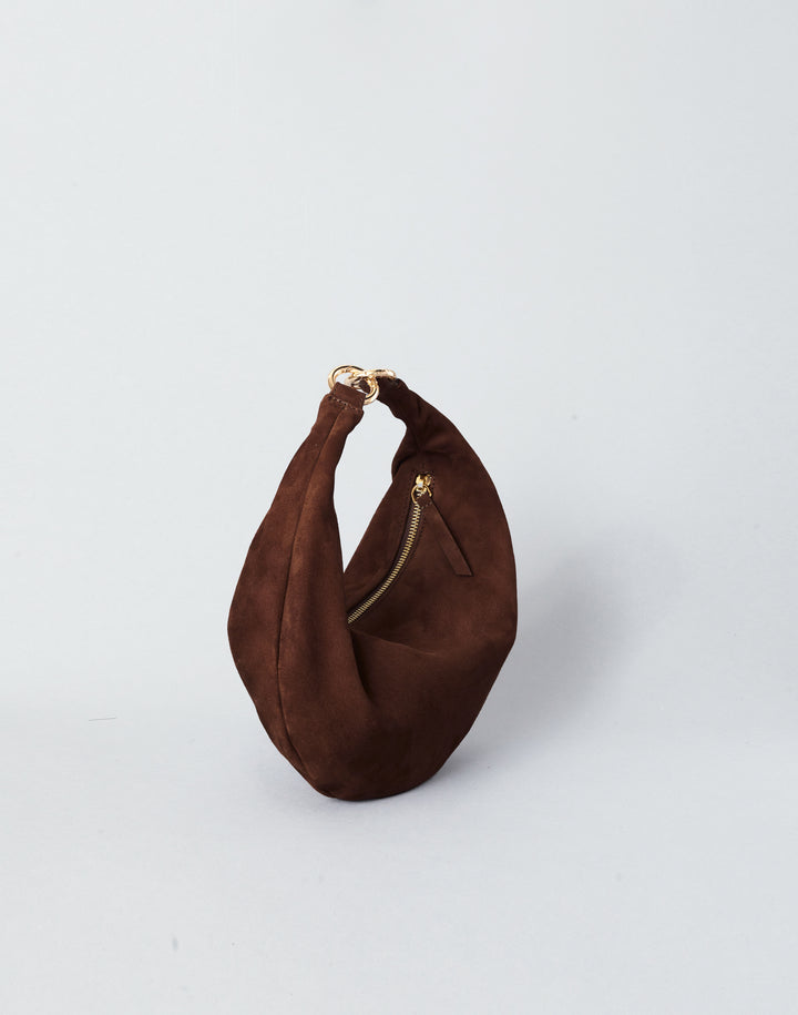 A dark brown suede crescent-shaped shoulder bag with a gold-tone zipper and ring hardware, photographed on a clean light gray background.#color_chocolate-suede