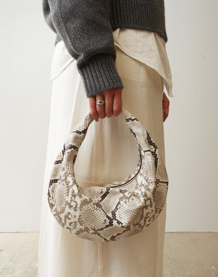 a woman in a grey sweater and cream pants holds a HYER GOODS convertible python crossbody hobo crescent bag Piccola ring bag #color_python-no-2