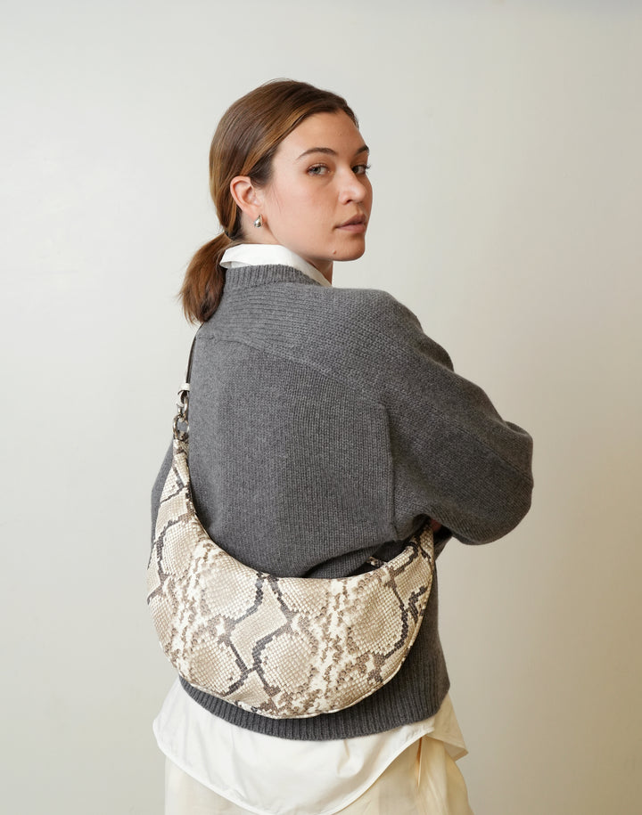 a woman in a grey sweater and cream pants wears a HYER GOODS convertible python crossbody hobo crescent bag Piccola ring bag #color_python-no-2