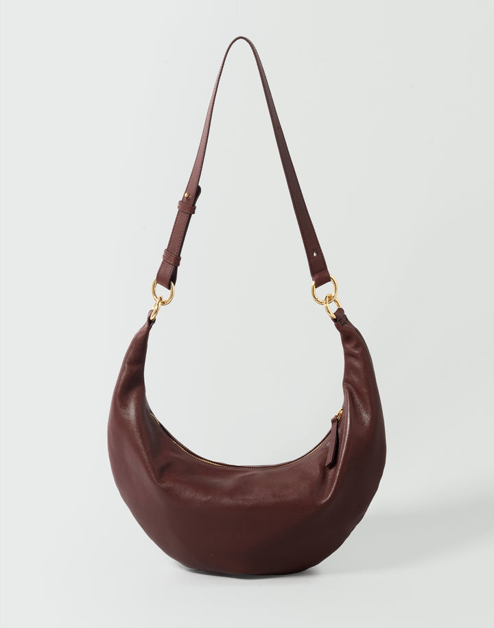 A burgundy leather crescent-shaped shoulder bag with gold-tone hardware and a matching adjustable shoulder strap, shown on a light gray background. #color_bordeaux-vintage