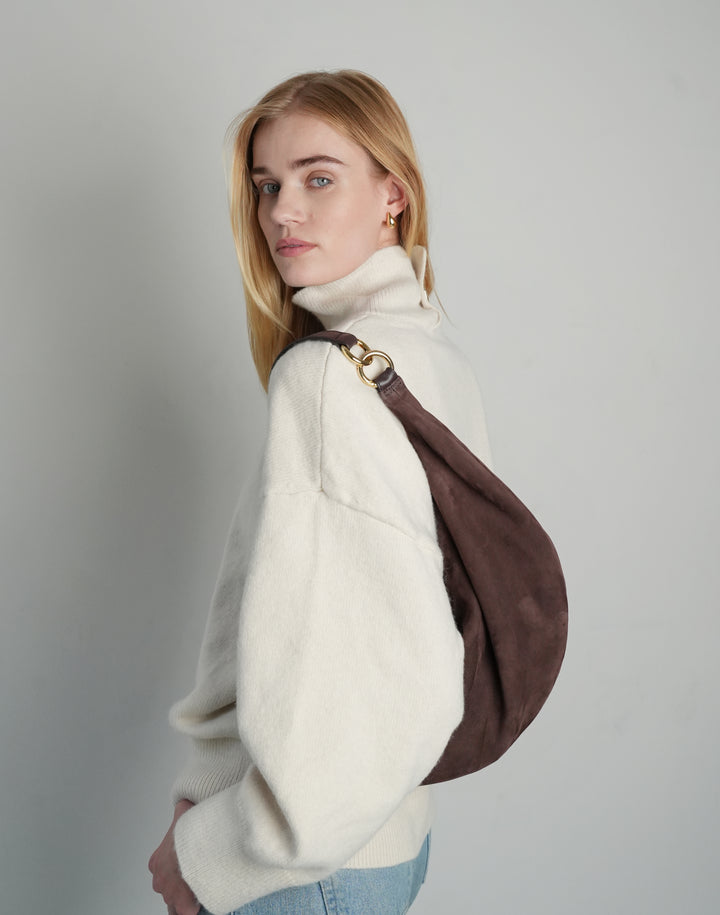 profile shot of a woman in an oversized cream sweater, light blue jeans, and a slouchy dark brown suede shoulder bag with gold hardware #color_chocolate-suede