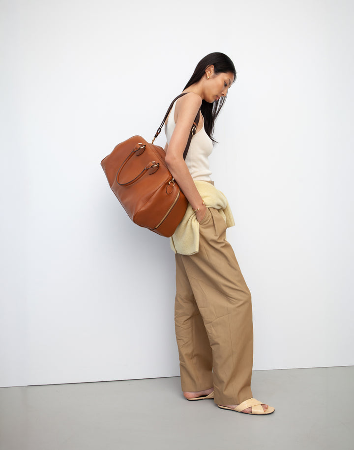 HYER GOODS tan leather la via weekender duffel bag held by model as shoulder bag #color_cognac
