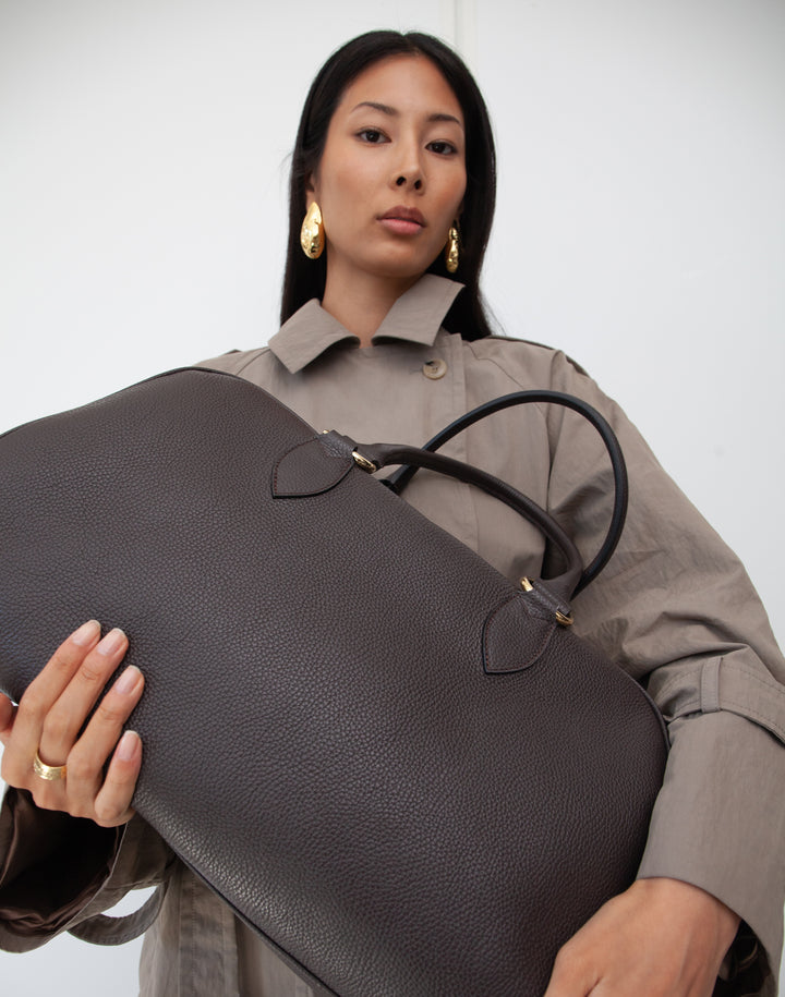 close up of HYER GOODS dark brown leather la via weekender duffel bag held by model #color_dark-chocolate