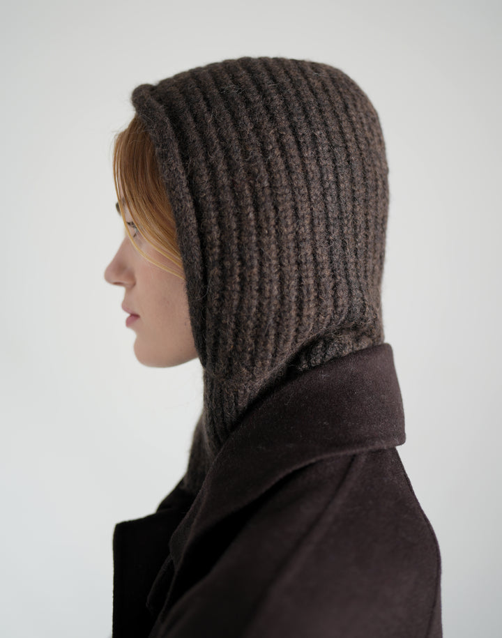 A side profile of a person wearing a dark brown ribbed knit hooded balaclava and a dark brown coat against a light gray background. #color_brown