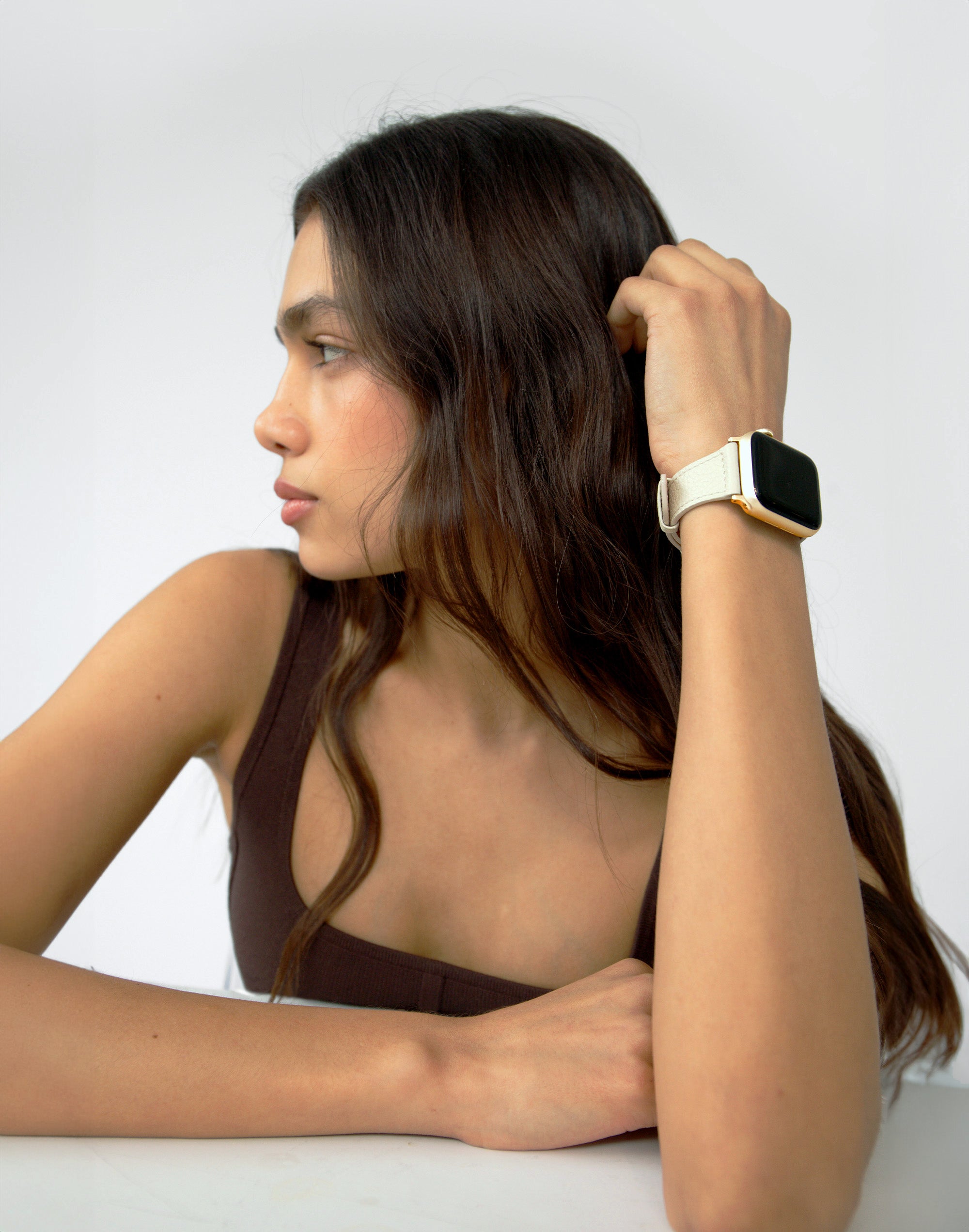 a women looks to the side, her left arm bent with an apple watch with a white leather band on her wrist