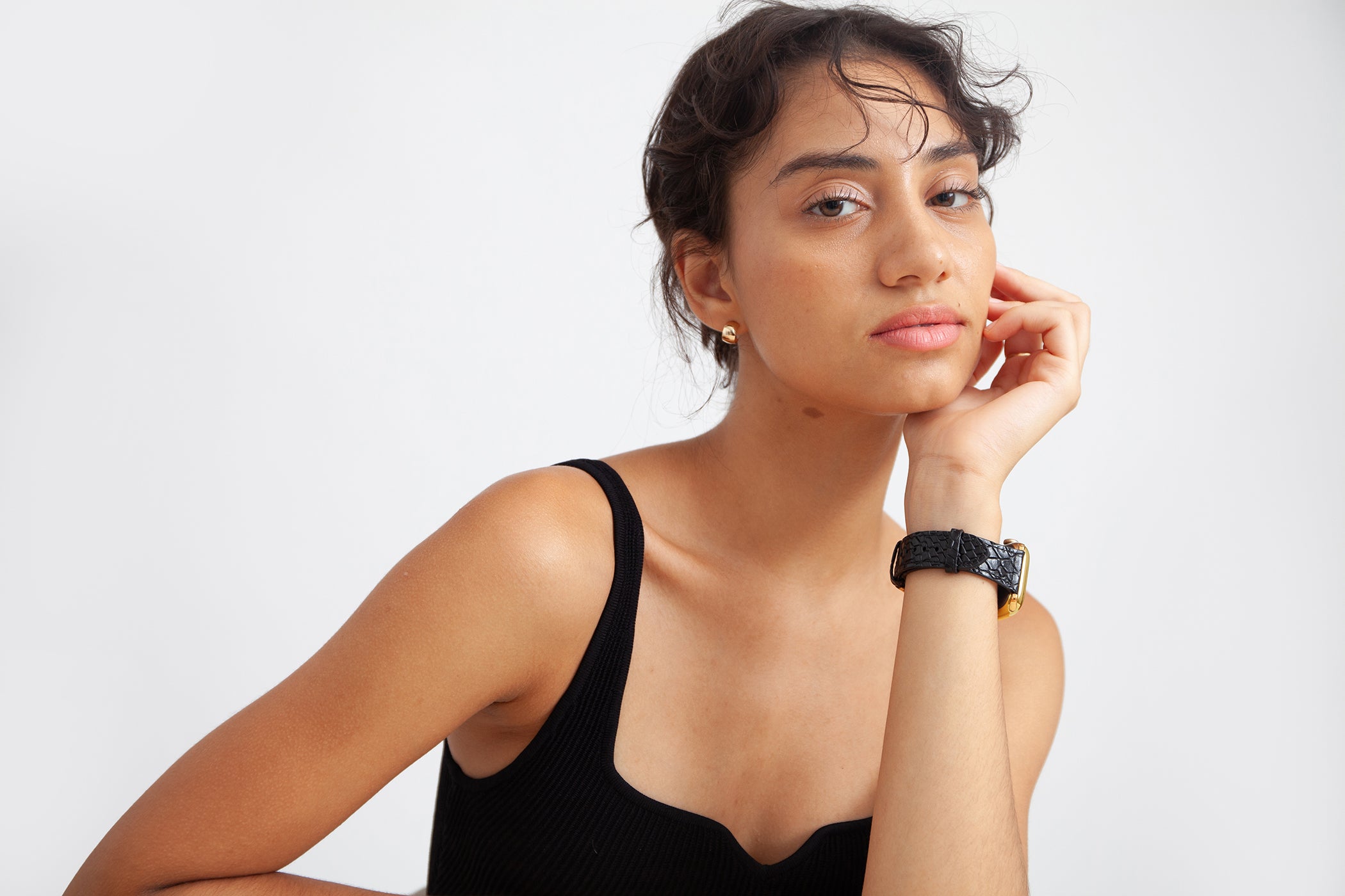 a girl leans her head on her palm, a black embossed watch band on her wrist