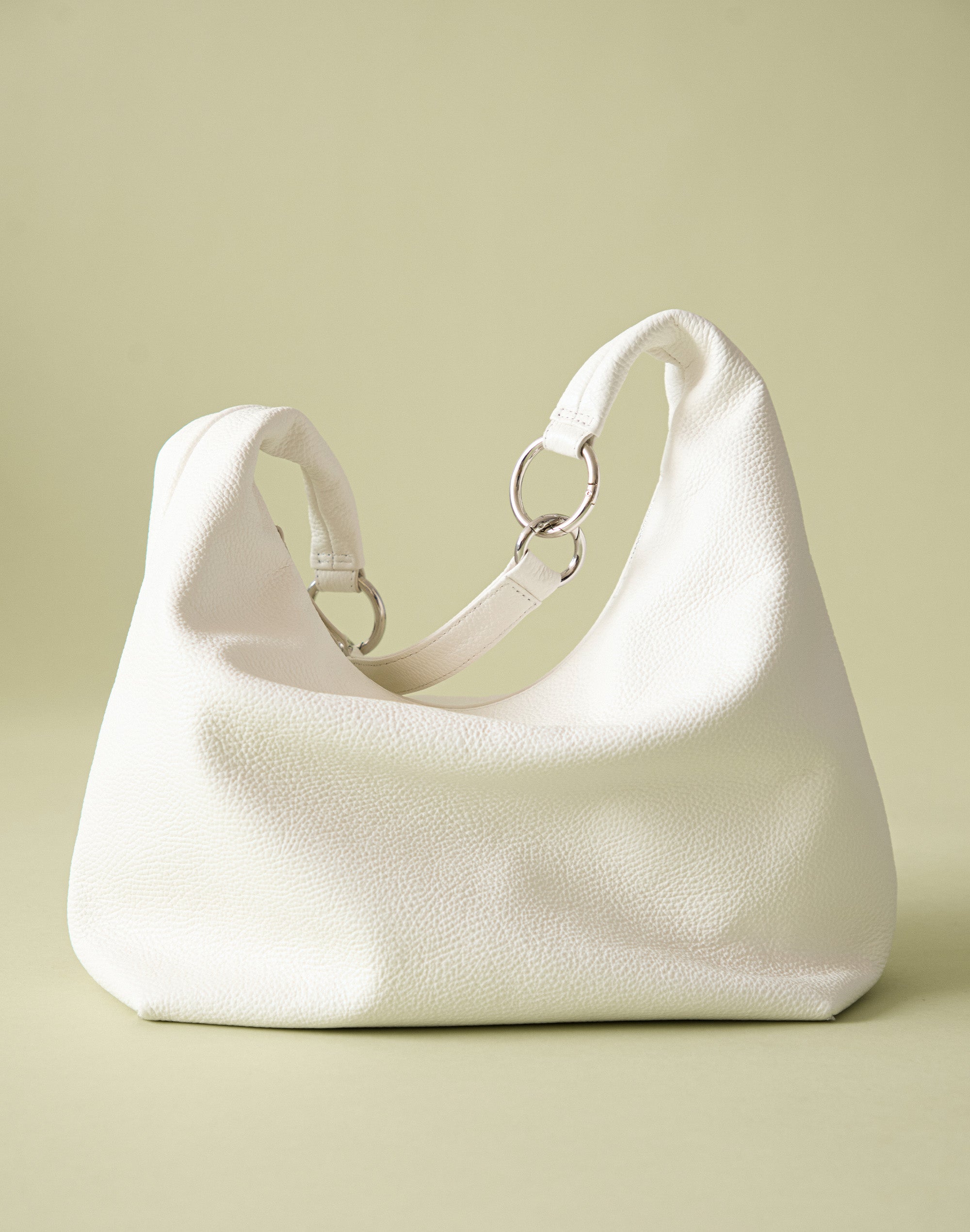a tumbled leather hobo bag in white with silver ring hardware. the soft, slouchy leather causes the strap to hang down.