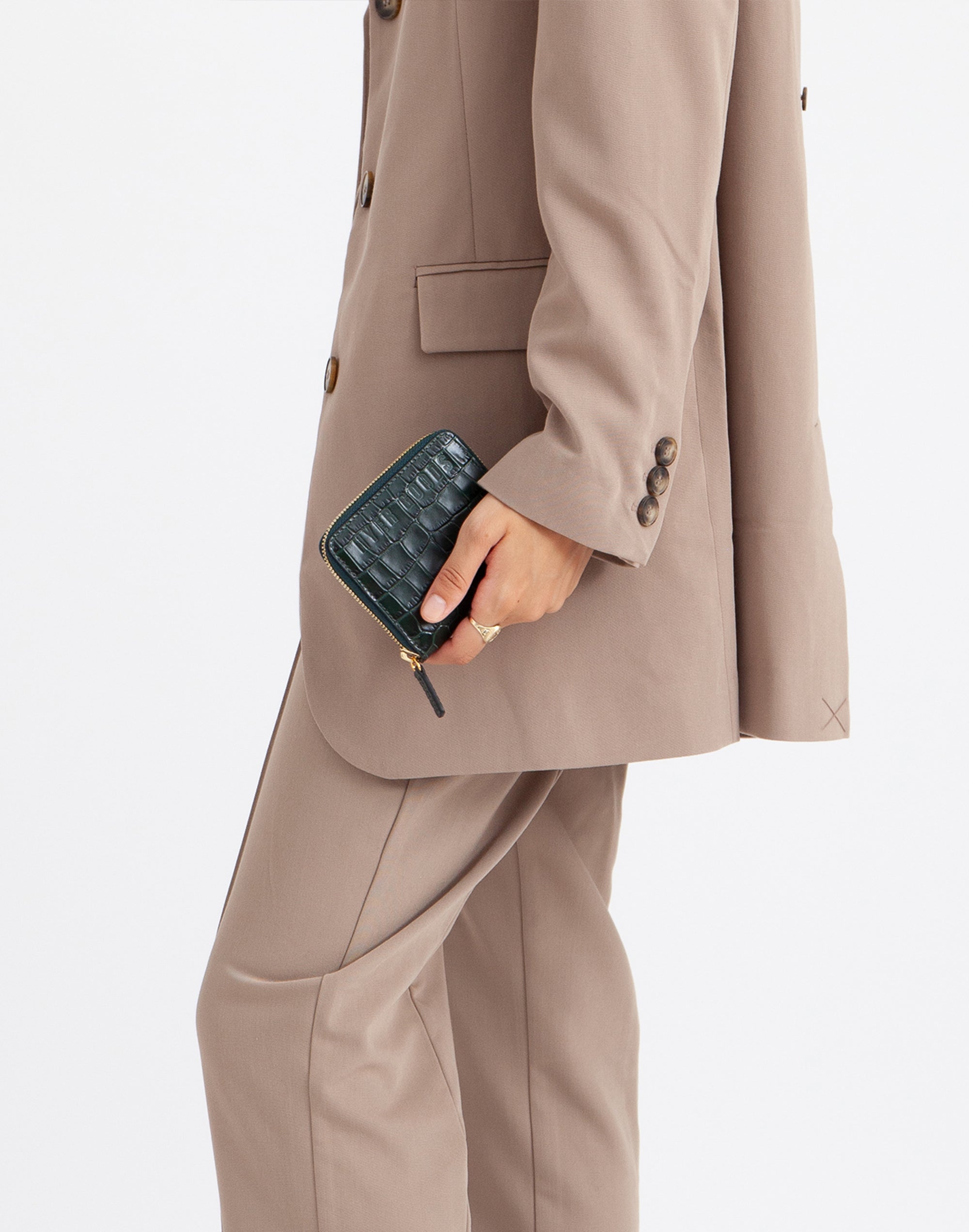 a person in a khaki suit clutches an emerald green croc zip wallet by their side