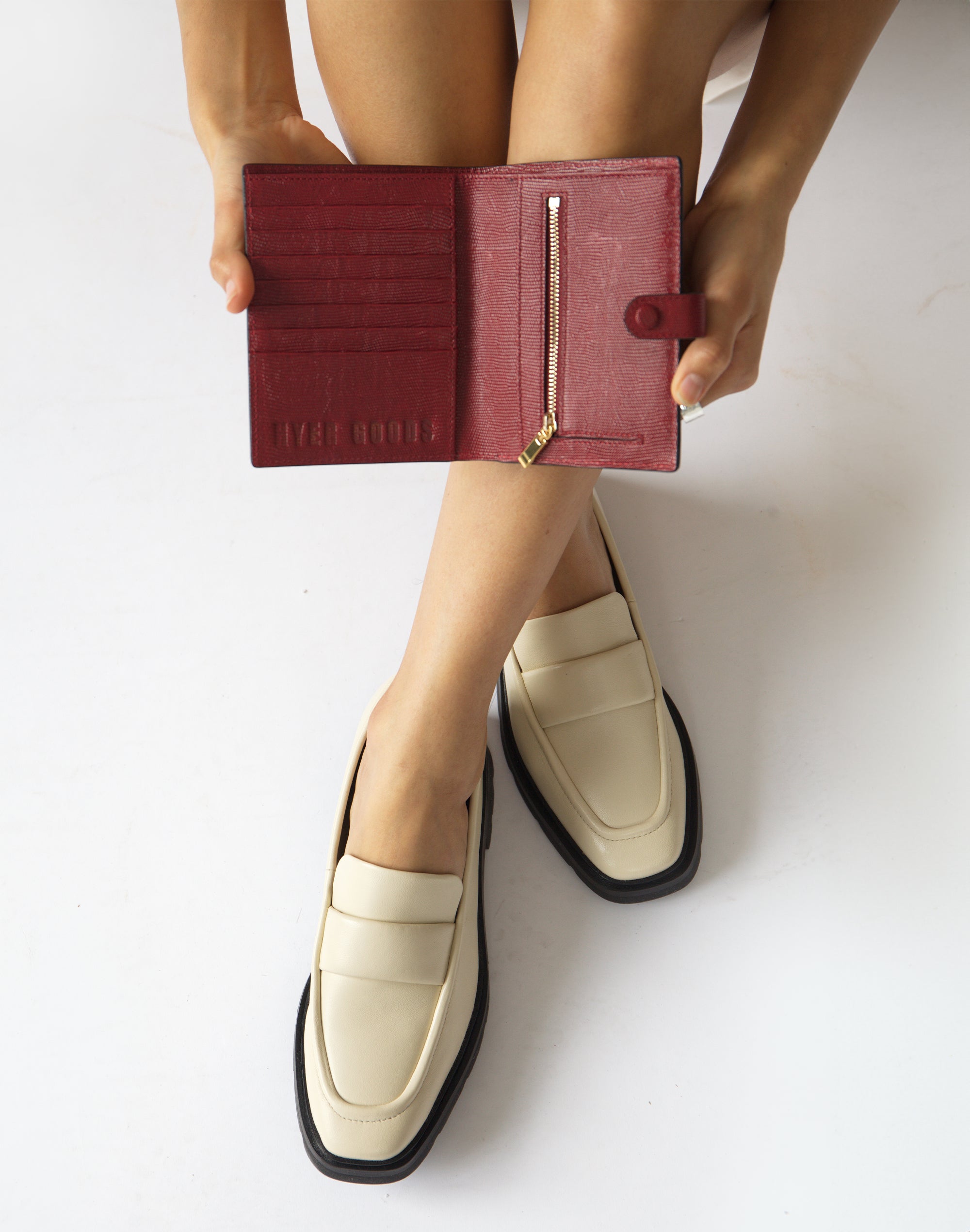 an overhead shot of someones shins, with a cherry red lizard wallet open on top with card pockets on the left and a gold zipper on the right